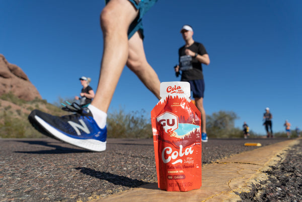 Runners stride past a red energy gel standing up by the side of the road.